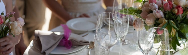 A close-up image of a table at a wedding reception with pink roses, wine, champagne glasses, and plates.