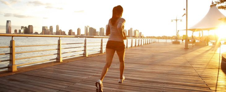 A young woman runs along the water at sunset