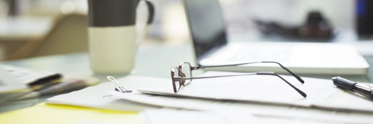 Financial papers, reading glasses, and laptop strewn about desk