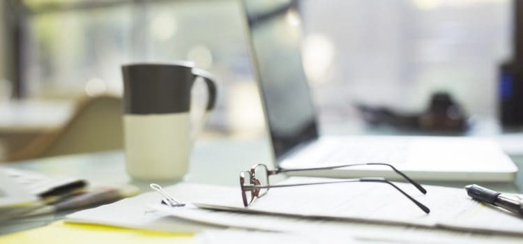 Financial papers, reading glasses, and laptop strewn about desk