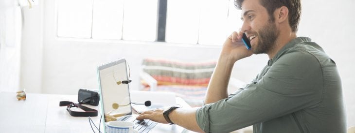 Man looking at his laptop, talking on his mobile phone