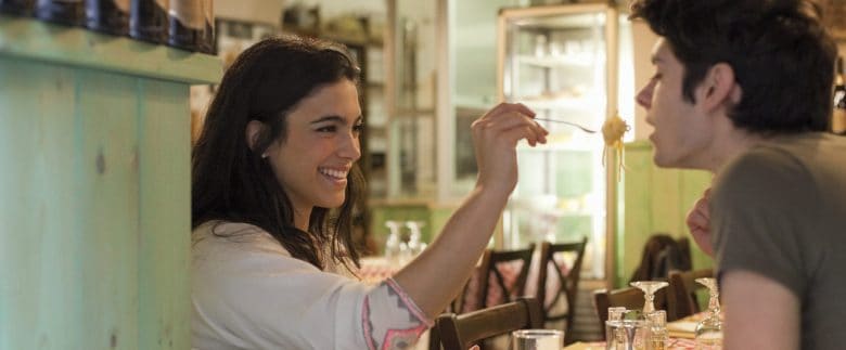 A woman feeds a forkful of pasta to a man, presumably her partner, at a restaurant.