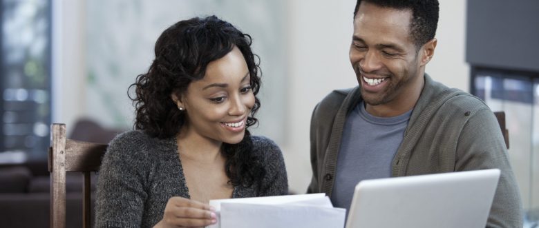 A man and a woman, both smiling as they sort through their household budget.