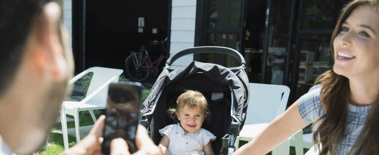 A dad takes a photo of a baby in a carrier while the mother smiles.