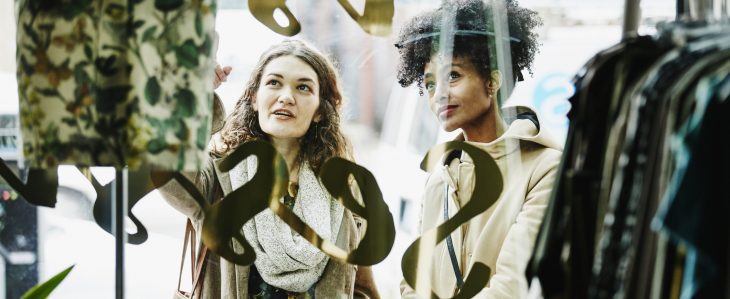 Two women commenting on a displayed garment as they window shop.