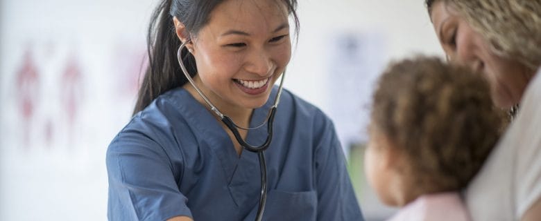 A smiling pediatrician meeting with a young patient and her mother.