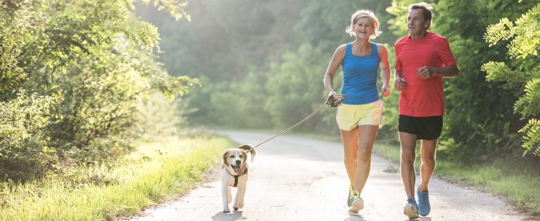 A middle aged couple jogging with their dog.