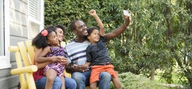 A mother and father with their son and daughter sitting on a bench outside.