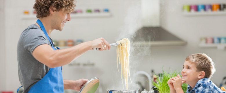 A man cooks pasta as his young son looks on.