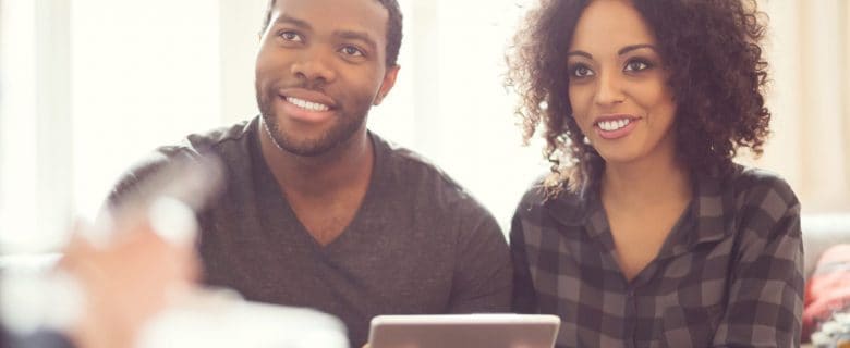 A man and a woman, sitting together on a couch, meet with a financial advisor.