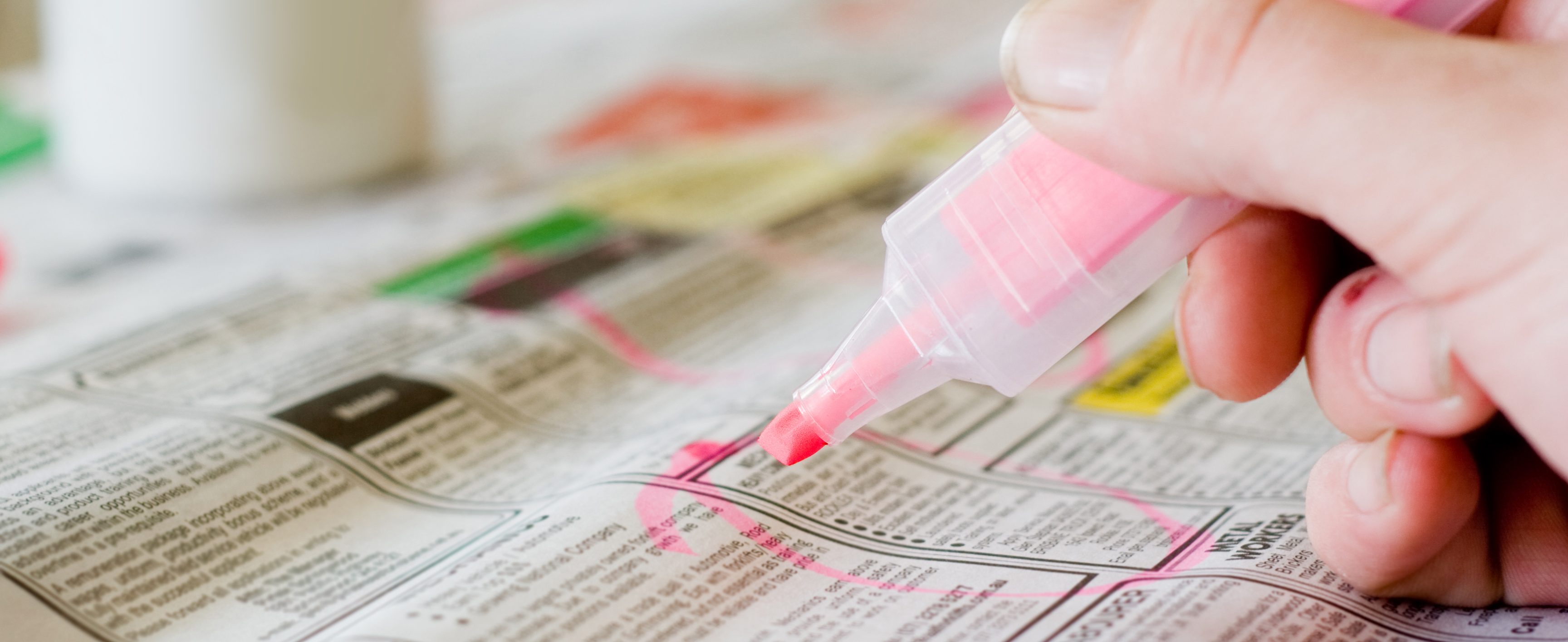 Close-up of someone circling items in a newspaper with a highlighter.