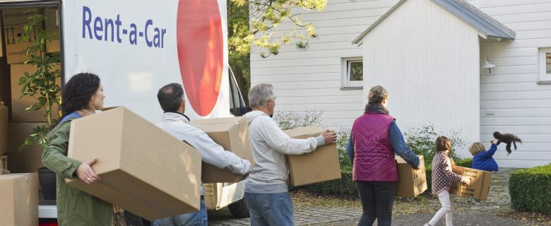 Members of a family carrying boxes from a moving van to their new home.