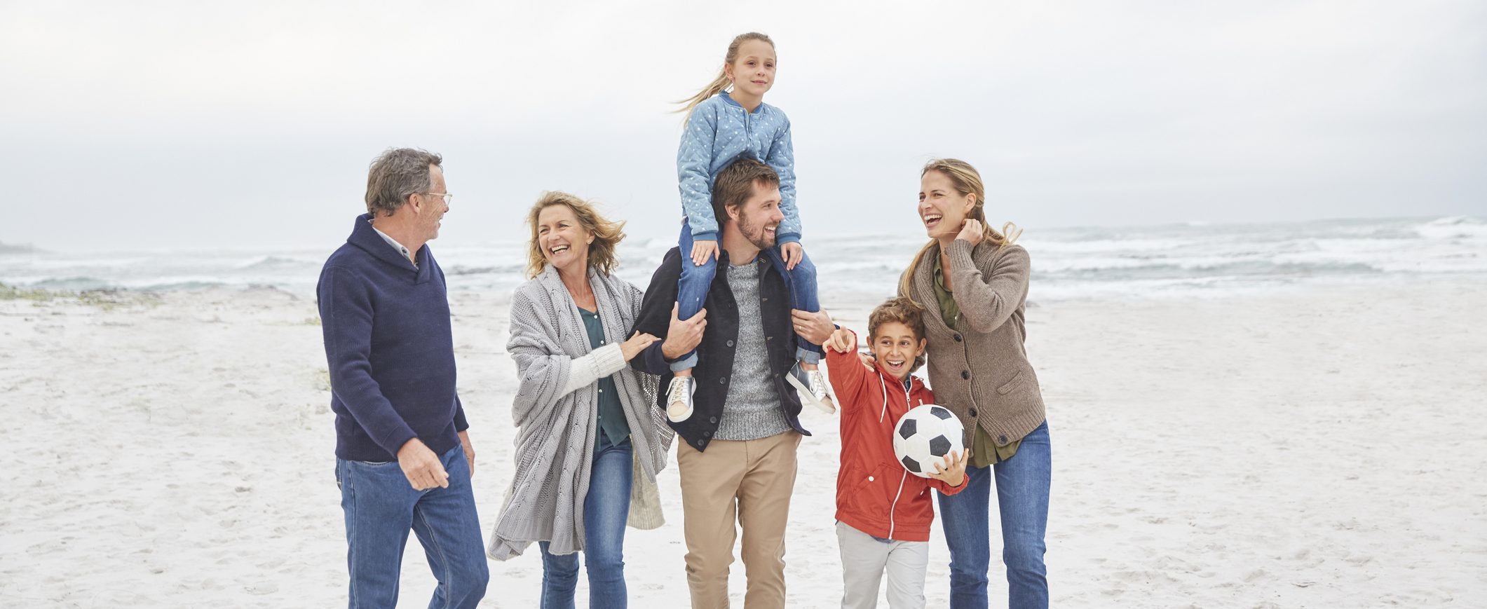 A family, including a grandmother, a grandfather, a   mom, a dad, and two children, walk on a beach together.