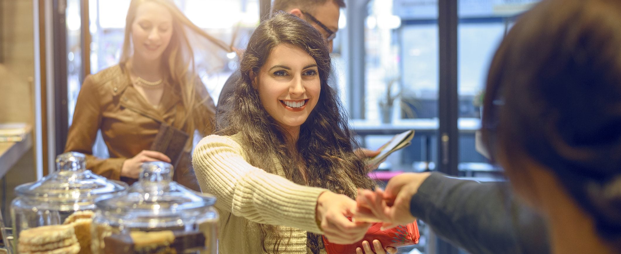 A smiling woman hands money to a cashier at a bakery.