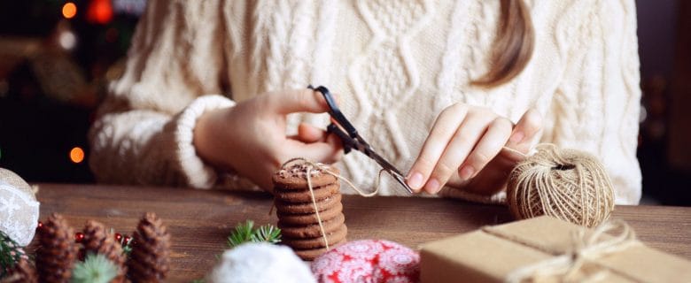 Closeup of a woman in a sweater wrapping holiday gifts.