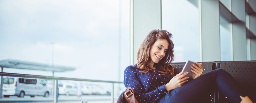 A woman sits on a bench and reviews her bank account on her tablet.
