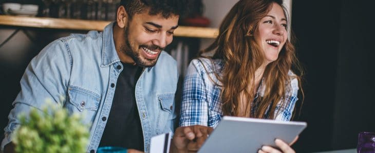 A smiling man and woman hold a tablet device.