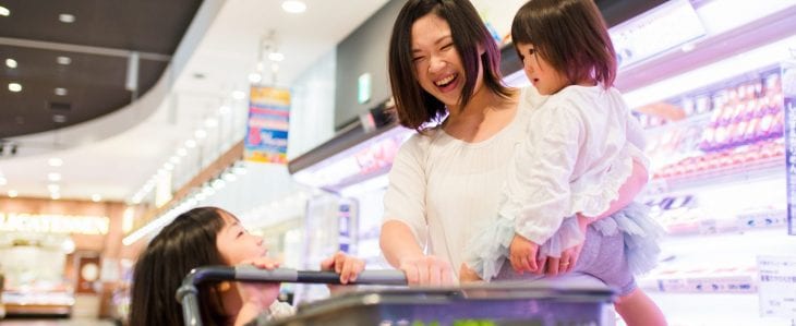 A smiling woman shops in a grocery store with her two small children.