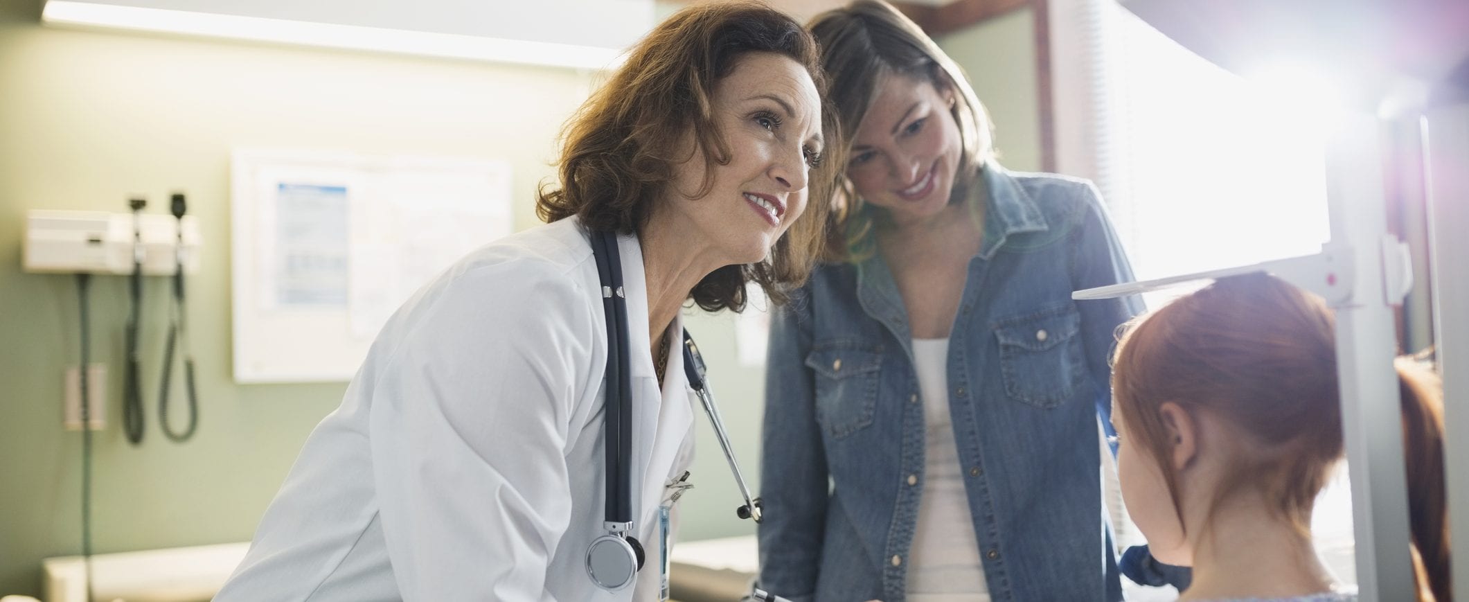 A young girl visits with her doctor, while her mother looks on.