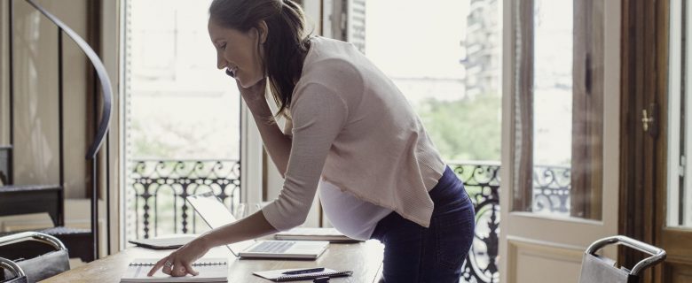 A pregnant woman makes plans, talking on the phone, while pointing at something in her appointment book.