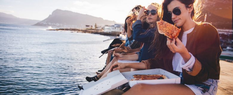 Friends sitting on a pier, eating pizza.