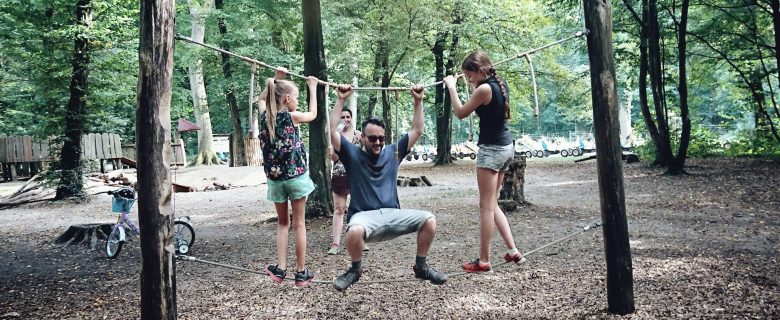 A man and his two daughters climb on ropes during a visit to a park.