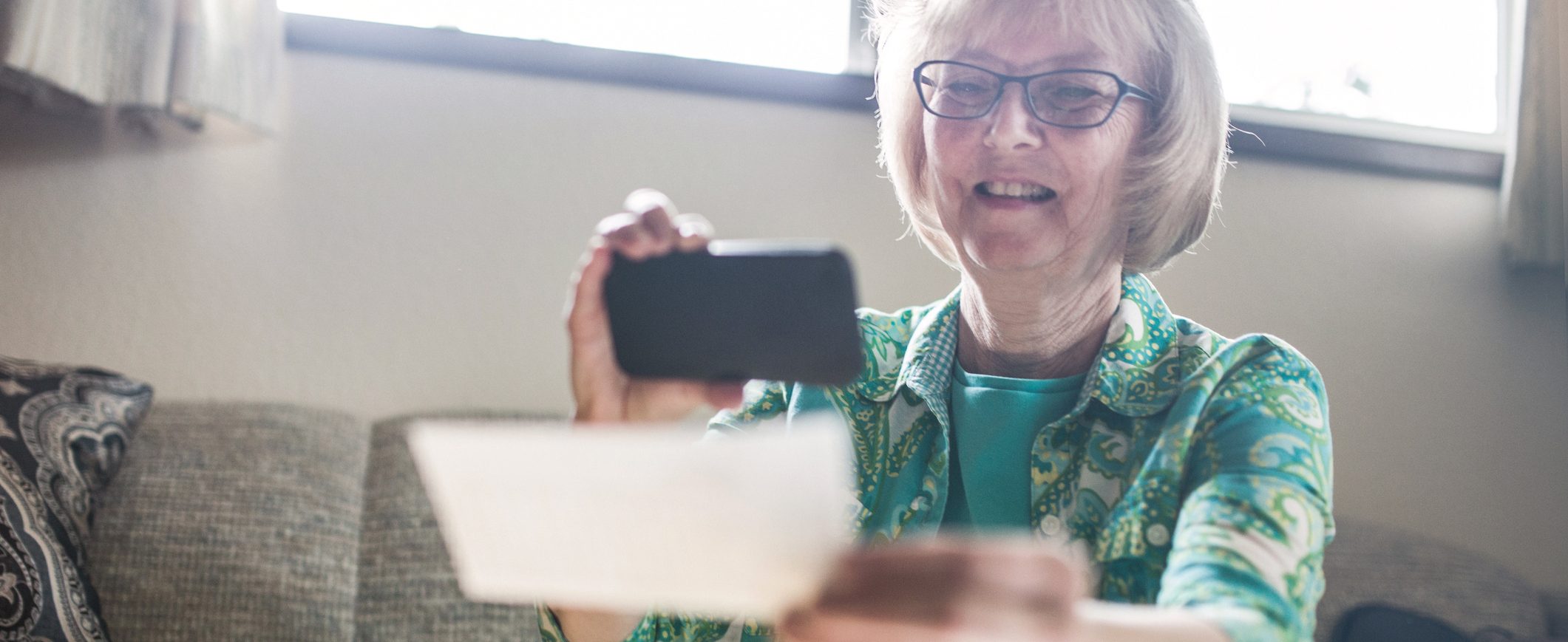 An older woman takes a picture of a check with her phone in order to use mobile check deposit.
