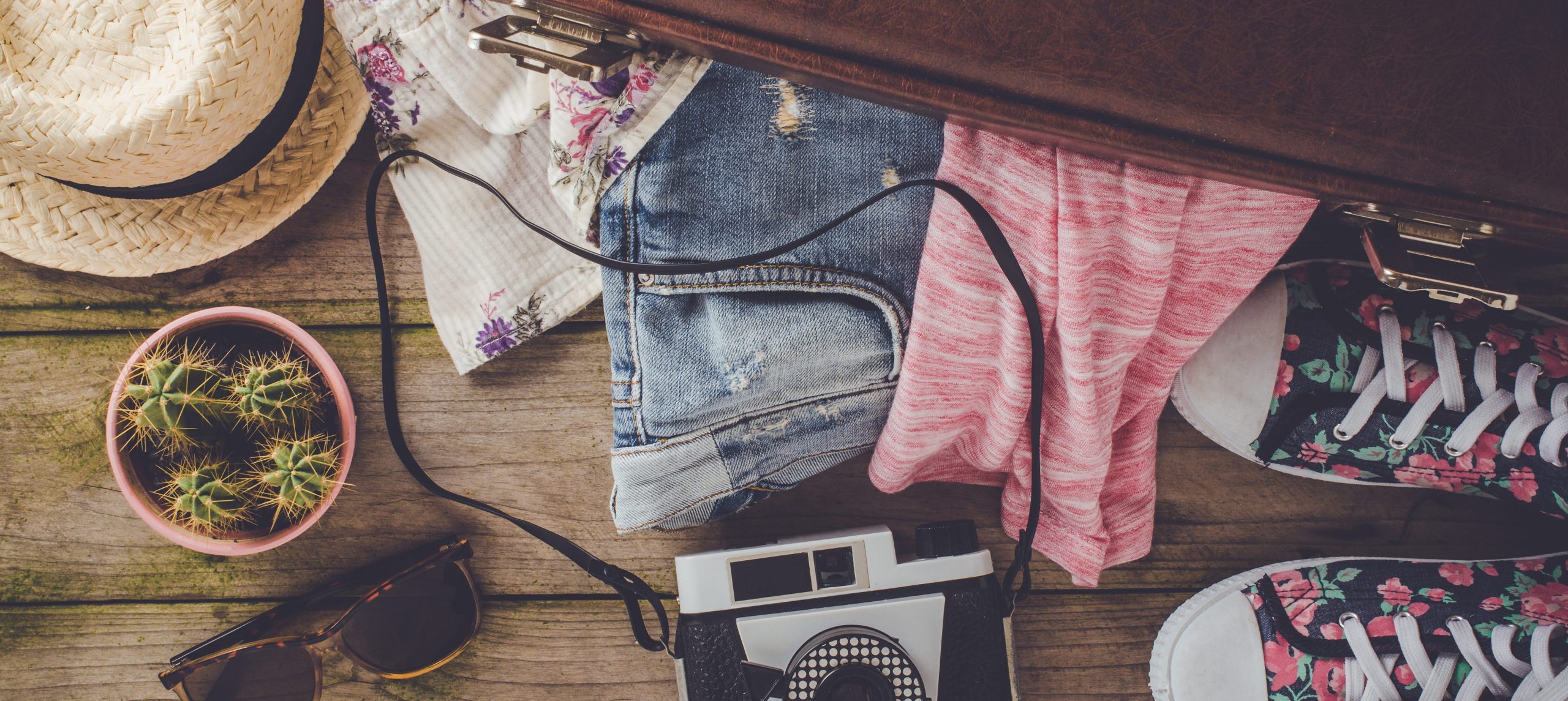 Vacation clothes, accessories, and a camera next to a suitcase.