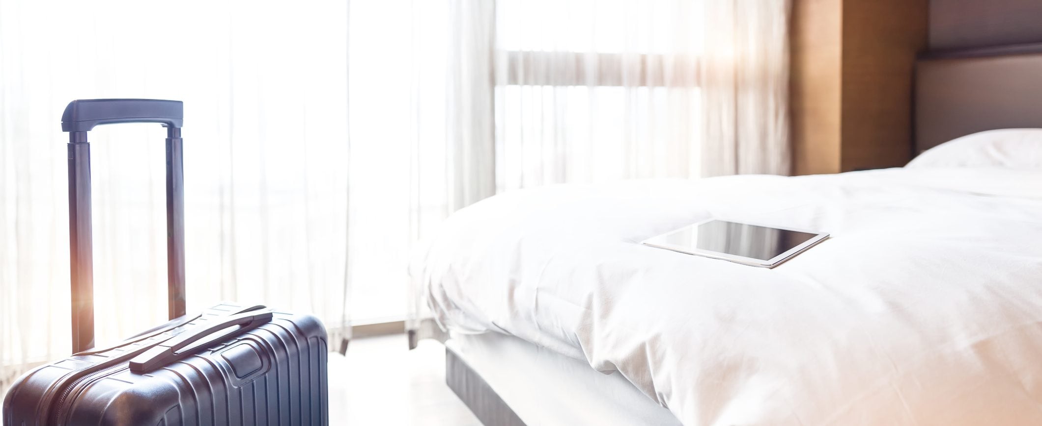 A suitcase in a hotel room with tablet laying on the bed.