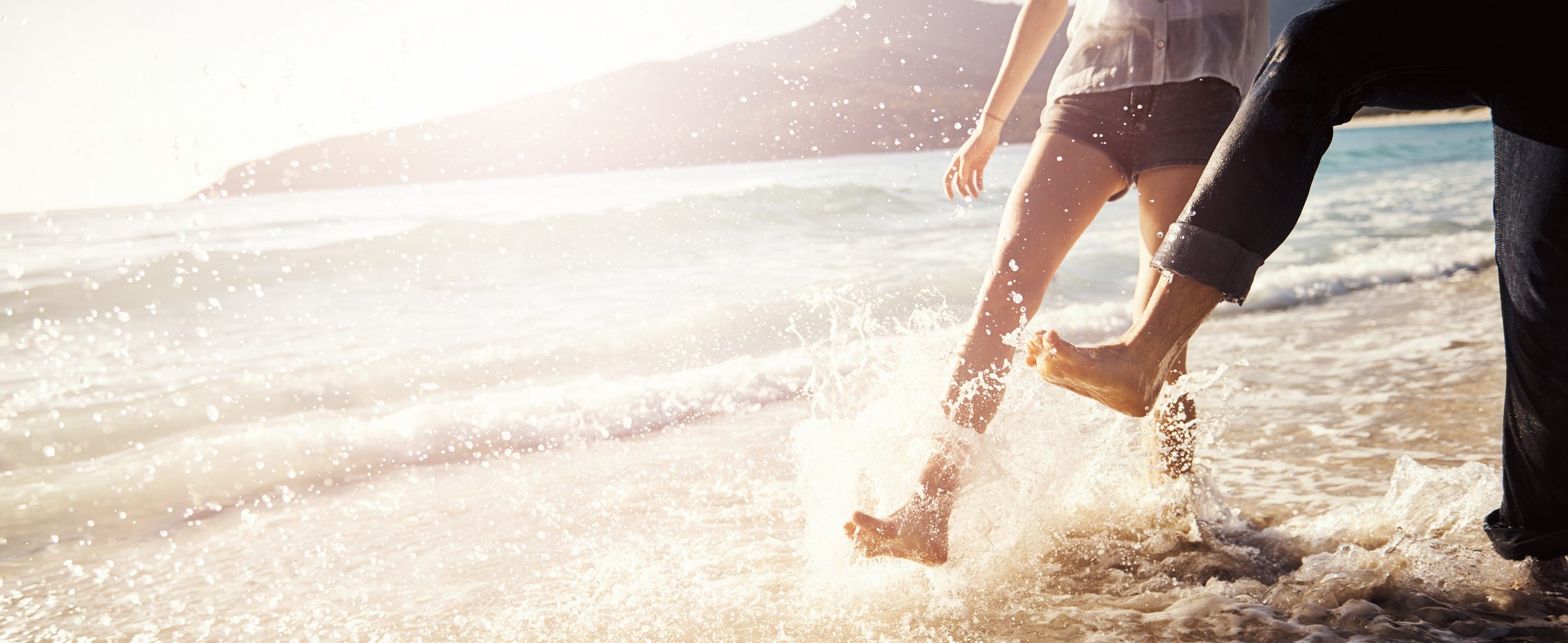 Two people kicking up water on a beach.