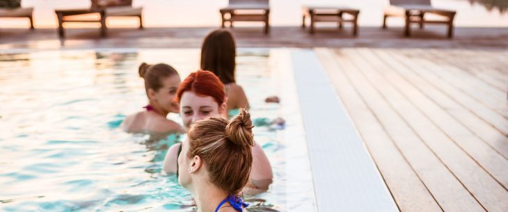 Four women hang out in an outdoor pool. 