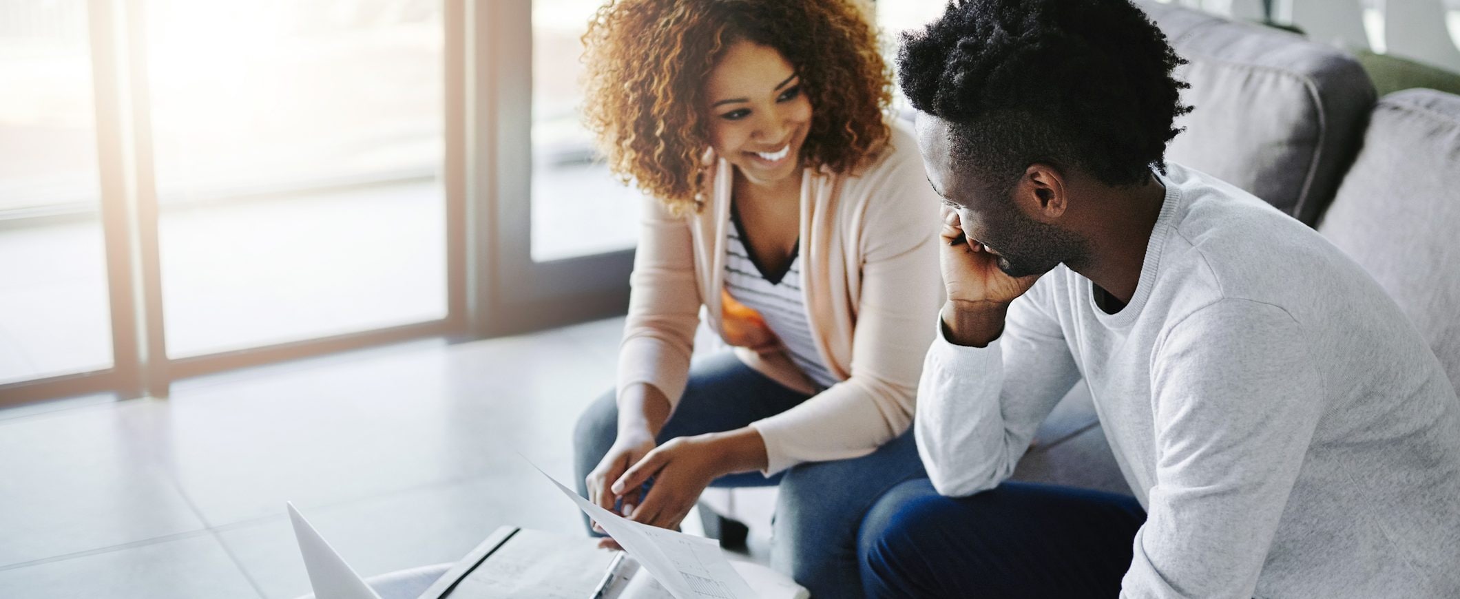 A couple sits on their couch and looks over financial paperwork.