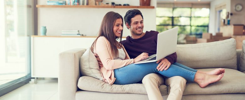 A man and a woman, snuggling on the couch and looking at their online savings account together.