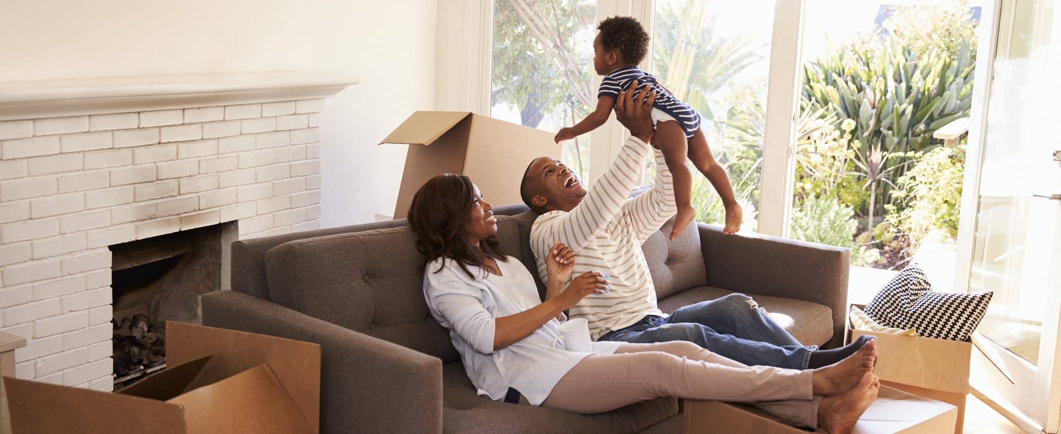 A man holding a baby and smiling, while sitting next to woman on a sofa.