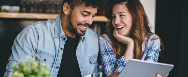 A man and woman smile at each other while the woman holds a tablet device.