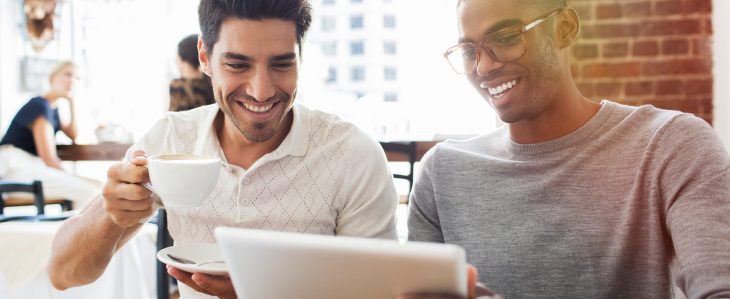 Two men in a coffee shop look at a tablet. 