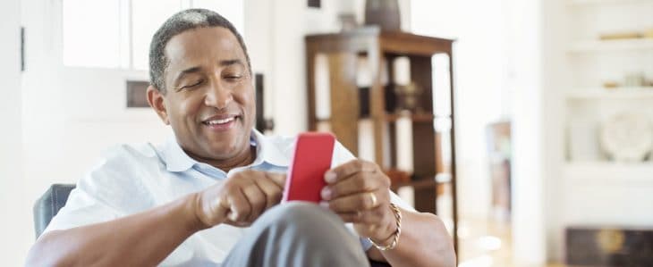 A man sitting in his home, using an app on his smart phone.