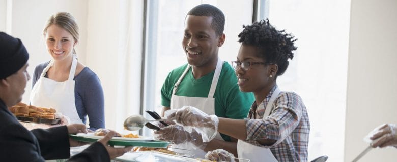 Three people stand in a line serving food to people in need. 