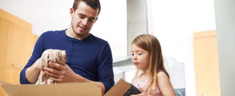A father and daughter pack a cardboard box together. 