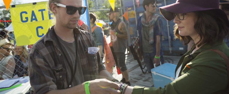 A worker at the entrance to a music festival puts a wristband on an attendee's wrist.