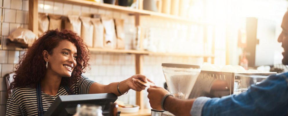 Woman smiling and handing her payment card to the cashier at a coffee shop.