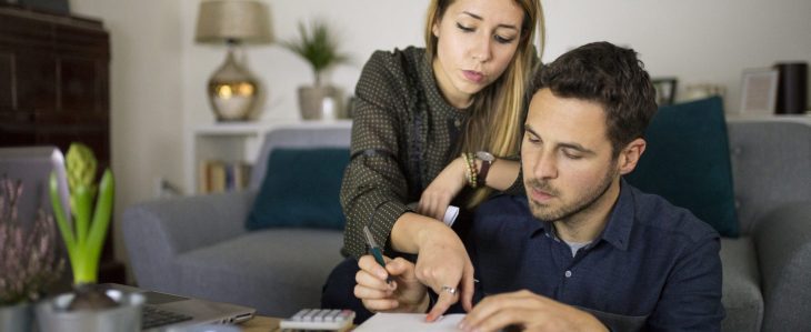 A man and a woman, sitting in their living room, go over their finances.