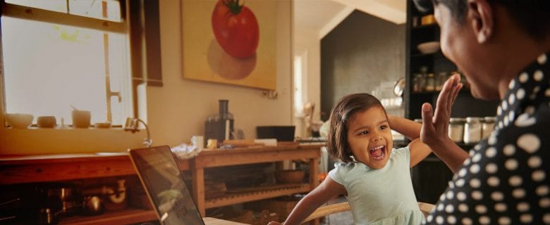 A man and his young daughter, in their kitchen, give each other a high-five after dad scores tickets to an amusement park.