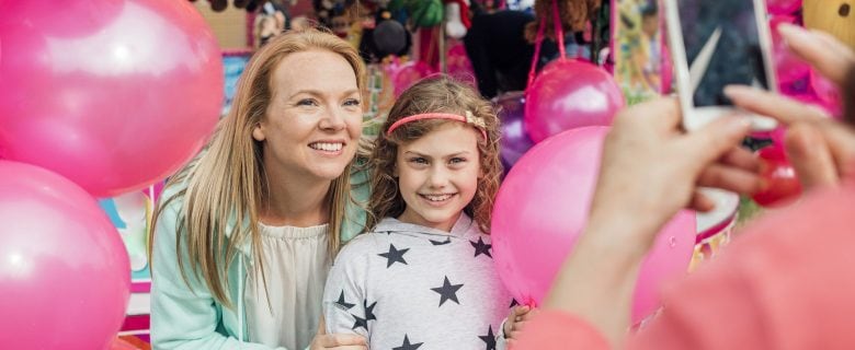 A woman and her daughter, at an amusement park, pose for a picture.