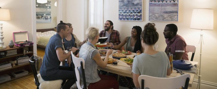 A group of seven friends sits around a table sharing dinner.