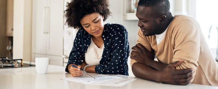 A man and a woman, sitting together in the kitchen, go over their finances. 