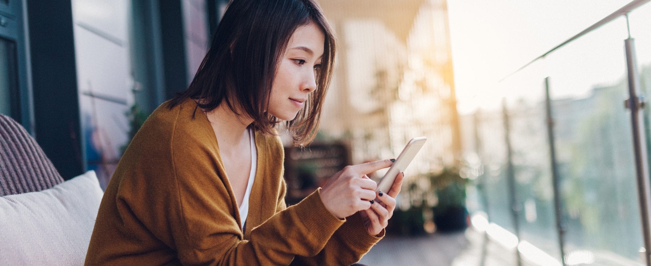 A woman sitting on her balcony, looking at her smart phone.