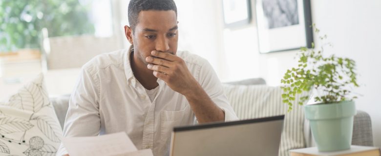 A man sits at a computer at home, looking at his billing statement.