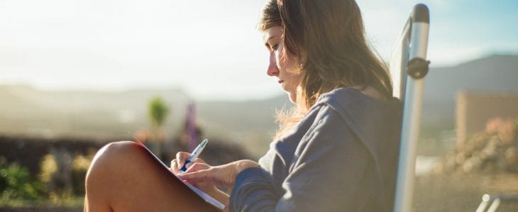 A woman sitting outside, writing in her notebook.