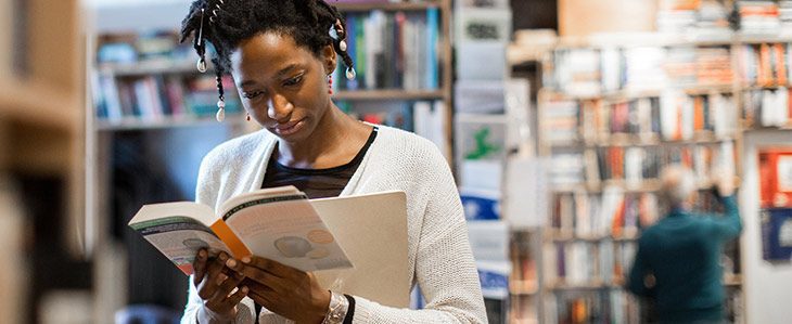 A woman, standing in a book shop, browses through a book.